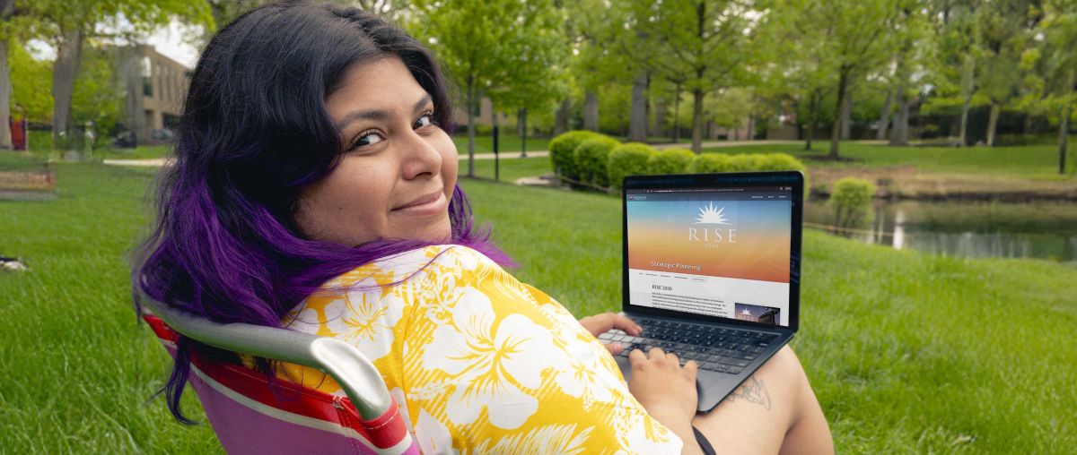 Quickpath student sitting by Lake Huntoon with laptop featuring RISE
