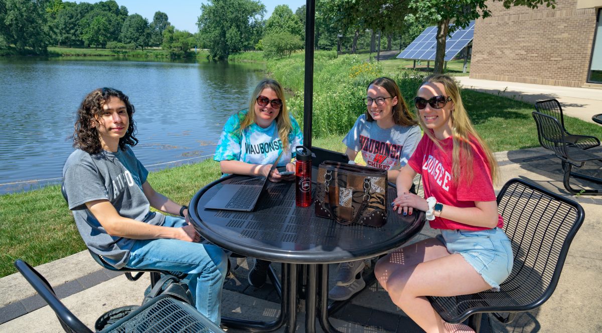 4 students sitting at table in front of lake huntoon in summer