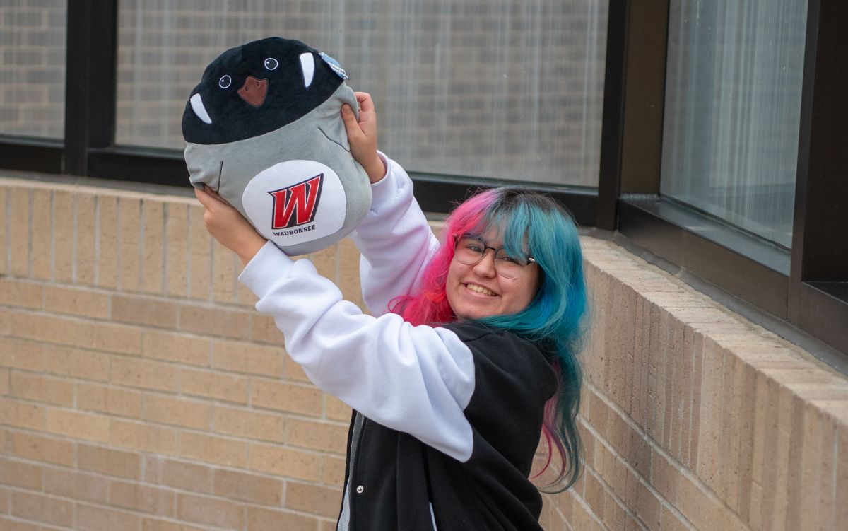 female student with multicolor hair holding a plush waubonsee branded toy