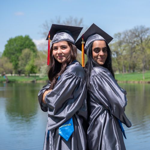 Quickpath Students in their graduation gowns and caps standing in front of Lake Huntoon