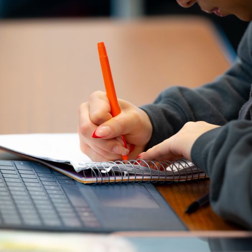 student writing / taking notes next to laptop