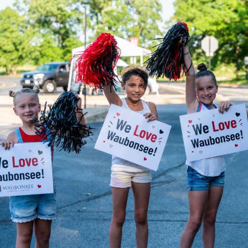 Three young people stand holding pom poms and signs that say "We Love Waubonsee"