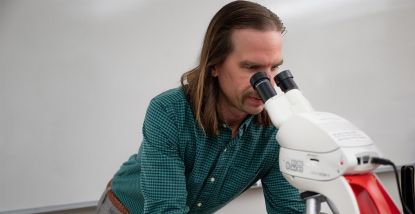 Dr. Evan Thomas - Assistant Professor of Biology looking through microscope