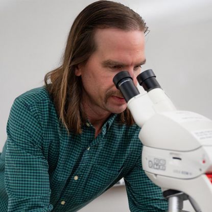 Dr. Evan Thomas - Assistant Professor of Biology looking through microscope