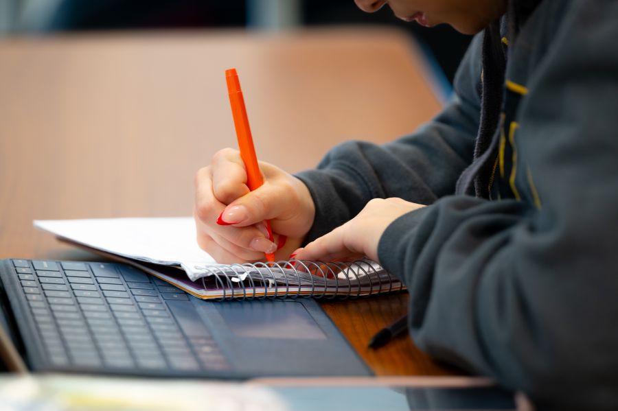 student writing / taking notes next to laptop